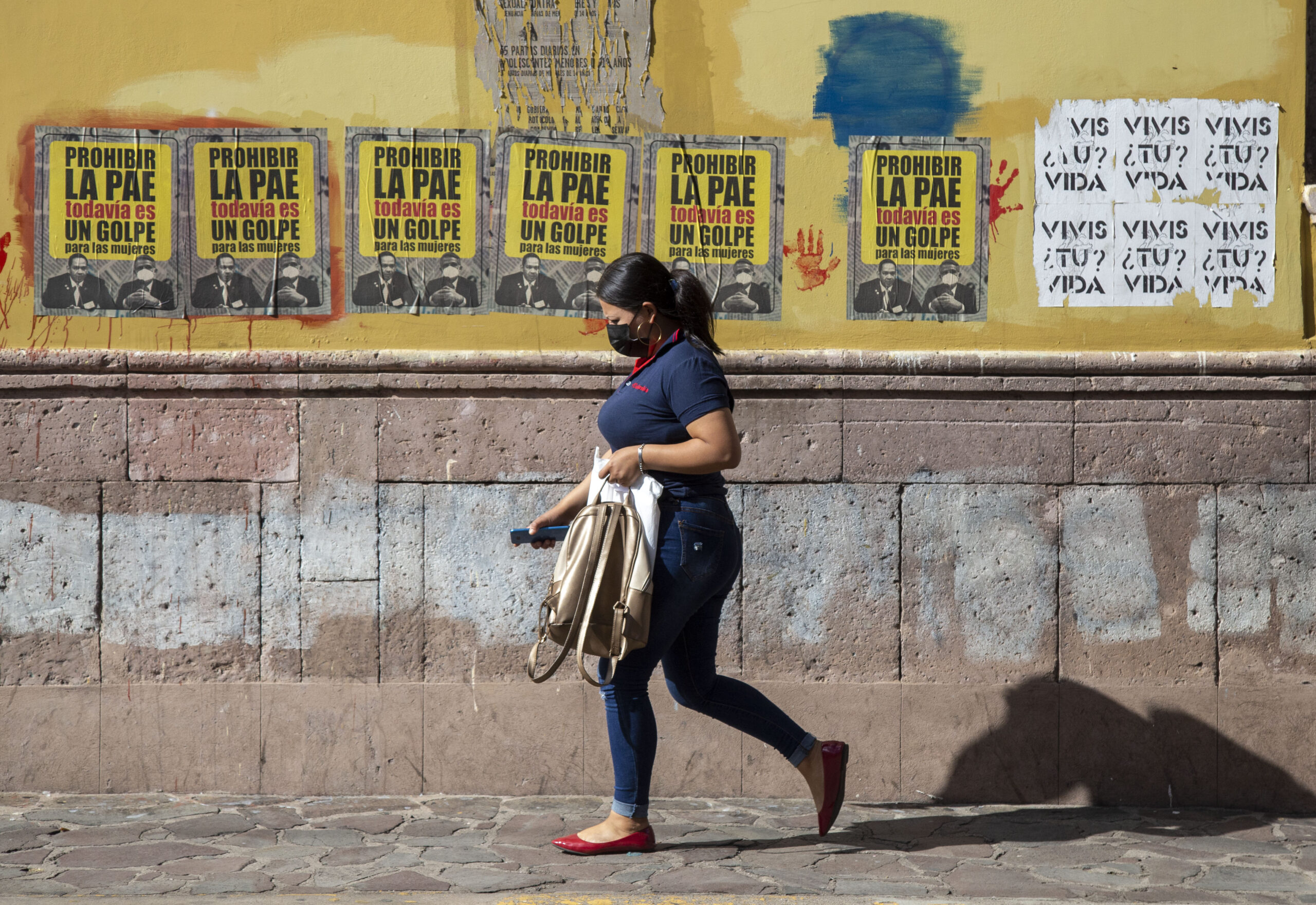 Mujer hondureña pasando delante de carteles sobre la píldora anticonceptiva de emergencia.
